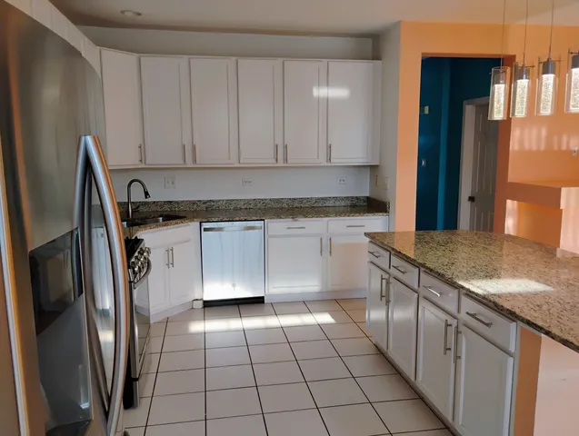 a kitchen with stainless steel appliances granite countertop a refrigerator a sink and white cabinets