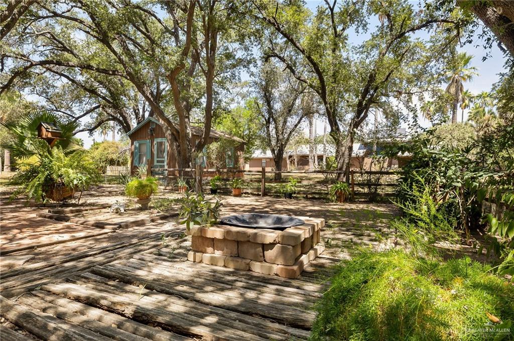 1803 North Bryan Road Mission, TX 78572 - Photo 21 of 30 Expansive outdoor space featuring a wood plank walkway, brick fire pit, and mature trees providing natural canopy