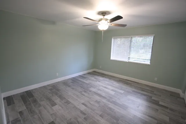 an empty room with wooden floor chandelier fan and windows