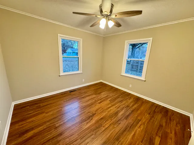 a view of an empty room with wooden floor and a window