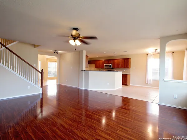 a view of a kitchen and an empty room with wooden floor and a ceiling fan