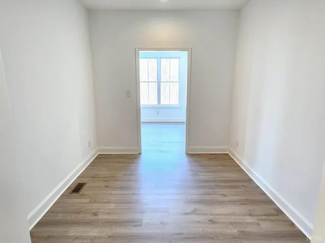 a view of an empty room with wooden floor and window