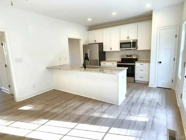 a kitchen with stainless steel appliances a stove top oven a sink a refrigerator white cabinets and wooden floor