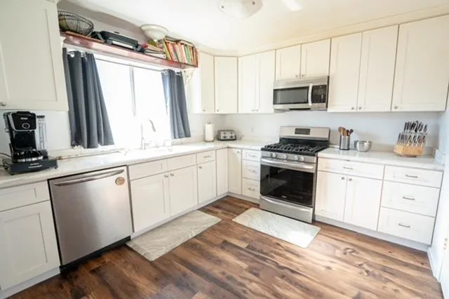 a white kitchen with stainless steel appliances granite countertop a stove a sink and white cabinets