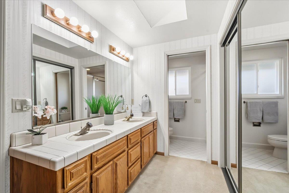363 Diamond Oaks Road Roseville, CA 95678 - Photo 24 of 51 The primary ensuite is filled with natural light from a skylight and window, featuring a dual-sink vanity, mirrored closet doors, and a separate shower and toilet area with a door.