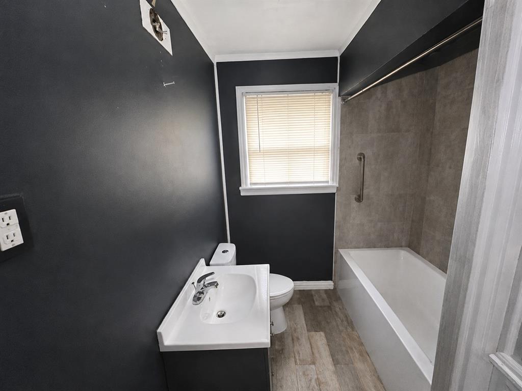 1010 Winters Street Dallas, TX 75216 - Photo 17 of 20 Bathroom featuring a single window, a white bathtub with a grab bar, large format wall tiles surrounding the tub, wood-finish flooring, and a vanity with an integrated sink