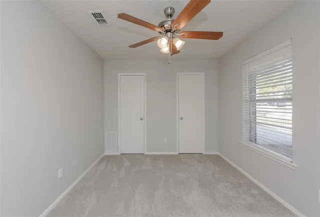 an empty room with a chandelier fan and windows