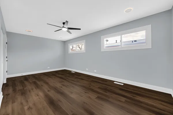 an empty room with wooden floor ceiling fan and windows
