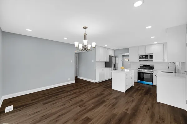 a view of an empty room and kitchen with wooden floor