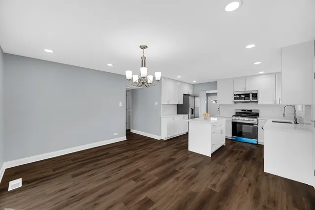 a view of an empty room and kitchen with wooden floor