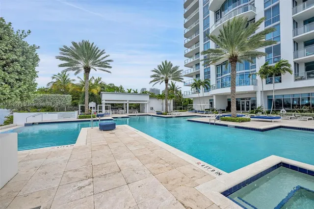 a view of swimming pool that has lawn chairs with plants and palm trees