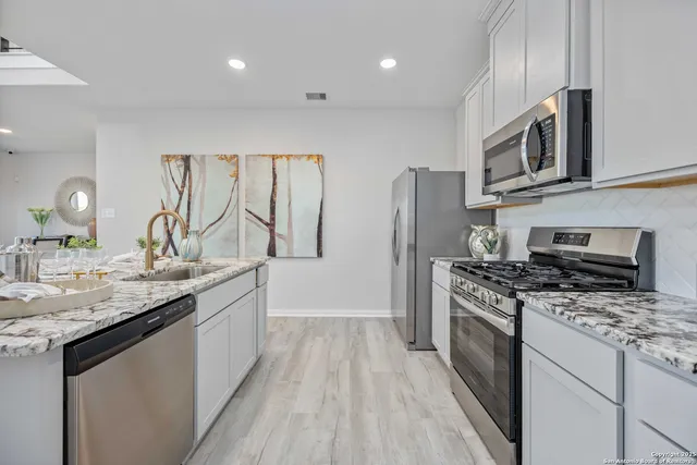 a kitchen with stainless steel appliances granite countertop a stove top oven a sink dishwasher a refrigerator and a microwave oven with wooden floor