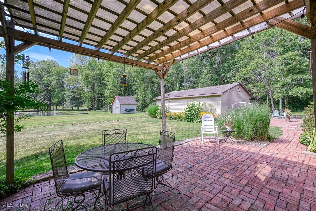 6640 Giddings Road Rootstown, OH 44272 - Photo 8 of 49 View of patio featuring outdoor dining space, a storage shed, view of wooded area, and a pergola