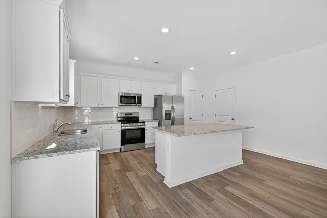 a large kitchen with stainless steel appliances kitchen island a stove a sink a refrigerator and white cabinets with wooden floor