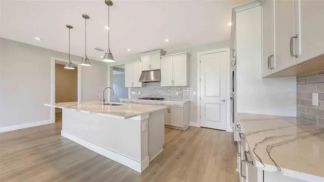 a large kitchen with kitchen island a stove a sink dishwasher a refrigerator and white cabinets with wooden floor