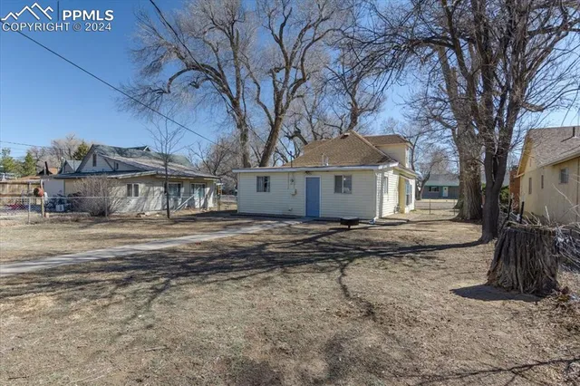 a view of a white house next to a road with large trees