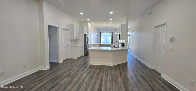 a view of an empty room and kitchen with wooden floor