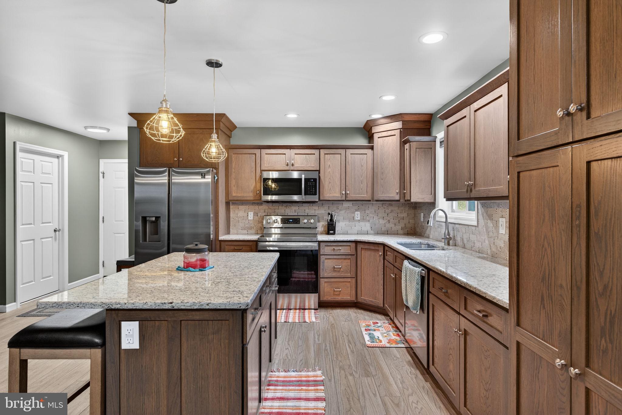 849 Sugar Run Road Millerstown, PA 17062 - Photo 9 of 34 a kitchen with stainless steel appliances kitchen island granite countertop a refrigerator a sink dishwasher and wooden cabinets with wooden floor