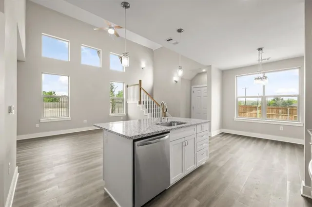 a kitchen with stainless steel appliances granite countertop a sink dishwasher a refrigerator and white cabinets with wooden floor