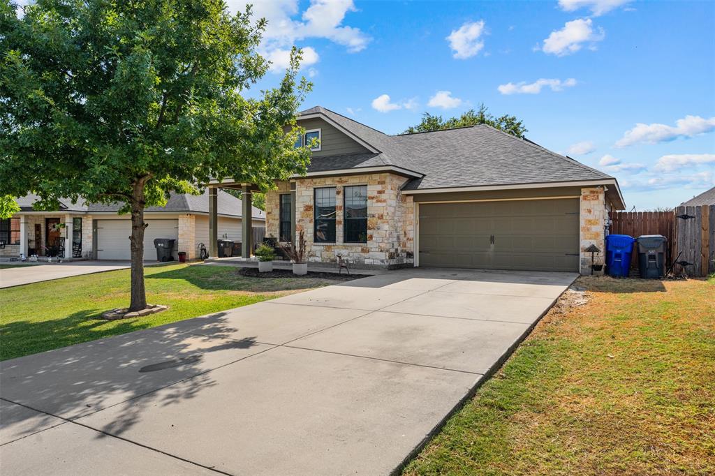 10313 Condor Loop Waco, TX 76708 - Photo 6 of 33 Stone veneer exterior with dark shingle roof, attached garage with a solid door, concrete driveway, and a front yard with mature trees