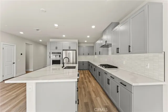 a kitchen with stainless steel appliances kitchen island a stove a sink a refrigerator and white cabinets with wooden floor