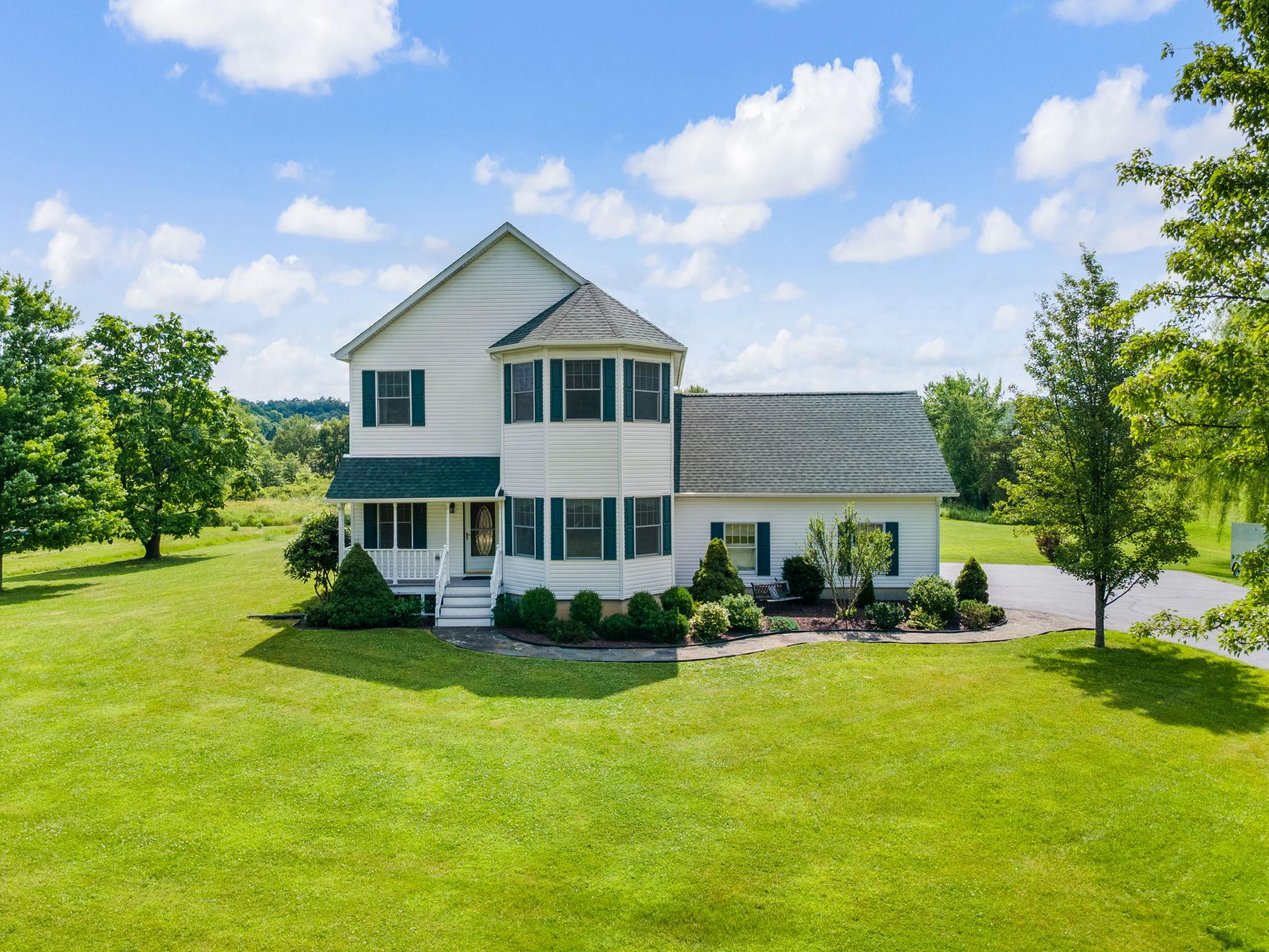 View of front facade with a front lawn, covered porch, and a shingled roof