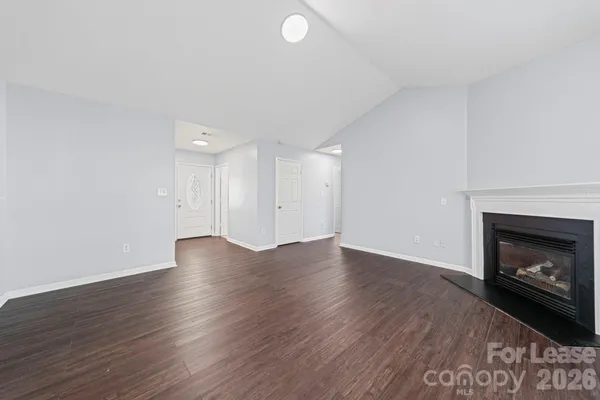 a view of an empty room with wooden floor fireplace and a window