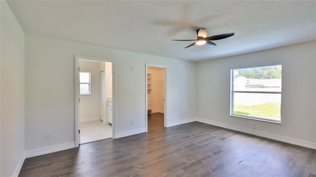 an empty room with wooden floor a ceiling fan and windows