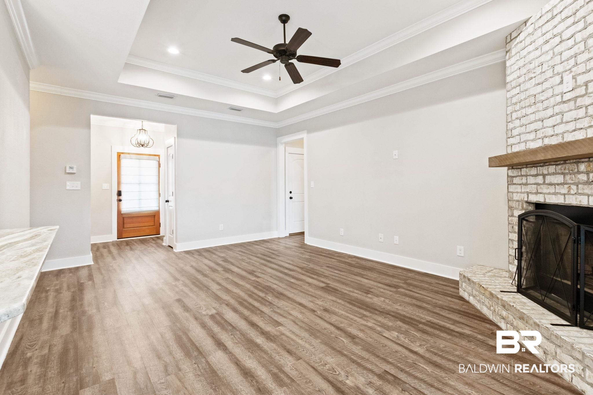 17376 Bankhead Boulevard Fairhope, AL 36532 - Photo 17 of 73 Unfurnished living room featuring a chandelier, wood finished floors, a brick fireplace, a ceiling fan, and ornamental molding
