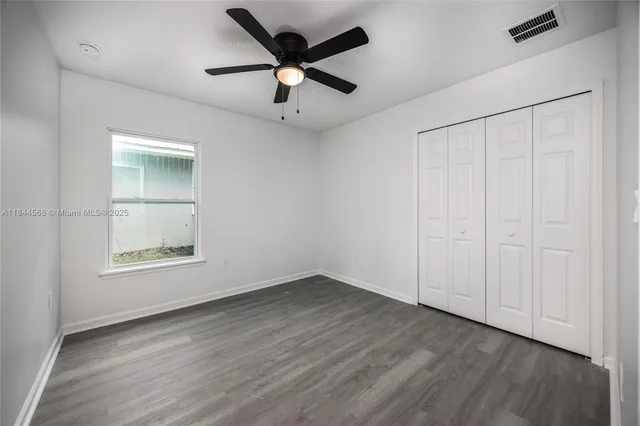 an empty room with wooden floor chandelier fan and windows