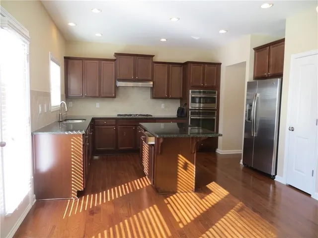 a kitchen with stainless steel appliances granite countertop a refrigerator a sink a stove and oven with wooden floor