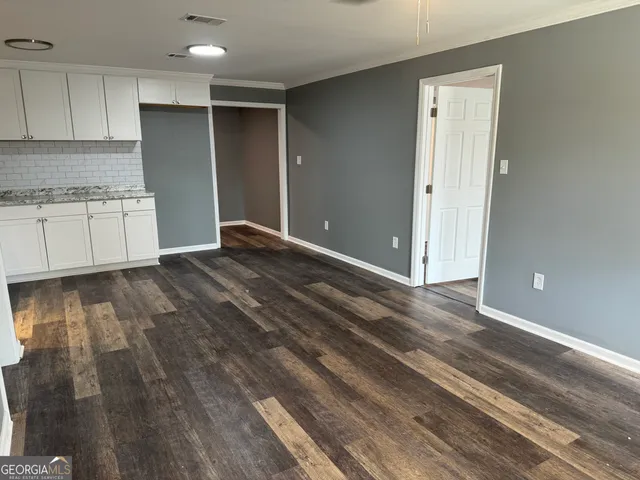 a view of an empty room with kitchen and window