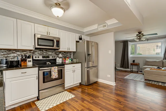 a kitchen with granite countertop a refrigerator a stove top oven a sink dishwasher and white cabinets with wooden floor