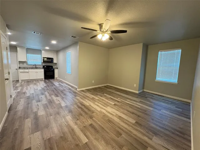 a view of an empty room with kitchen appliances and a ceiling fan