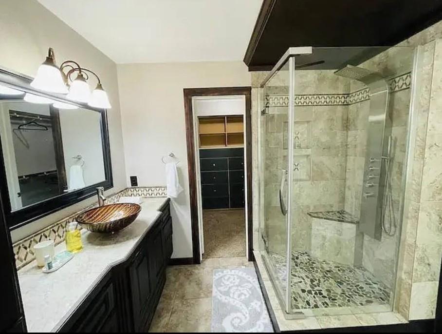 207 Emberson Chapel Road Pilot Point, TX 76258 - Photo 9 of 18 Custom vessel sink with an extensive vanity, fully-tiled shower with a built-in bench, shower panel system, and glass enclosure, and an adjacent walk-in closet