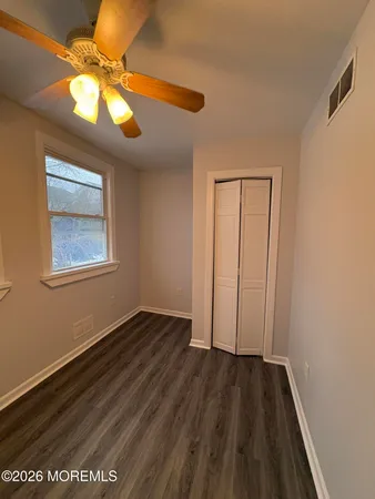 a view of an empty room with wooden floor and a chandelier fan