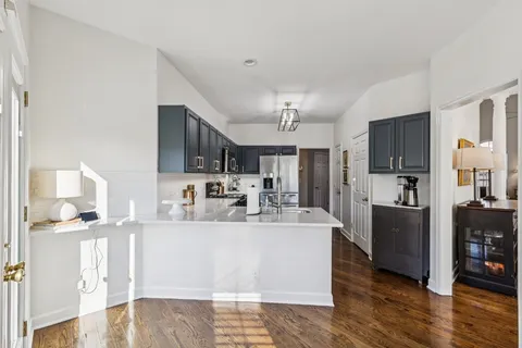 a large white kitchen with stainless steel appliances kitchen island granite countertop a refrigerator a stove a sink and a dining table with wooden floor