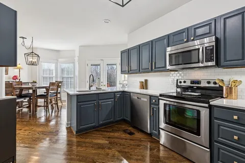 a kitchen with stainless steel appliances granite countertop a stove top oven a sink dishwasher a dining table and chairs with wooden floor