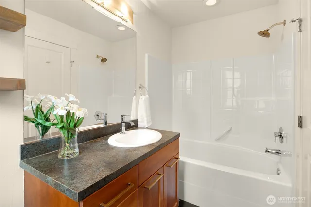 a bathroom with a granite countertop sink a mirror a bathtub and shower