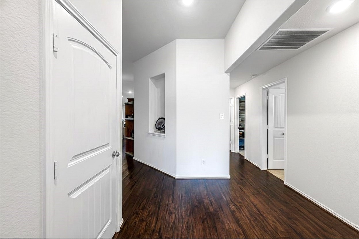 17439 Chester Valley Trail Hockley, TX 77447 - Photo 5 of 22 This photo showcases a bright hallway with sleek dark wood flooring, white walls, and multiple doorways leading to other rooms. The space is modern and inviting, offering easy access to various parts of the home.