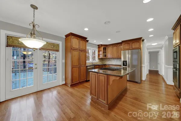 a kitchen with stainless steel appliances granite countertop a refrigerator a sink dishwasher a stove and a wooden floor
