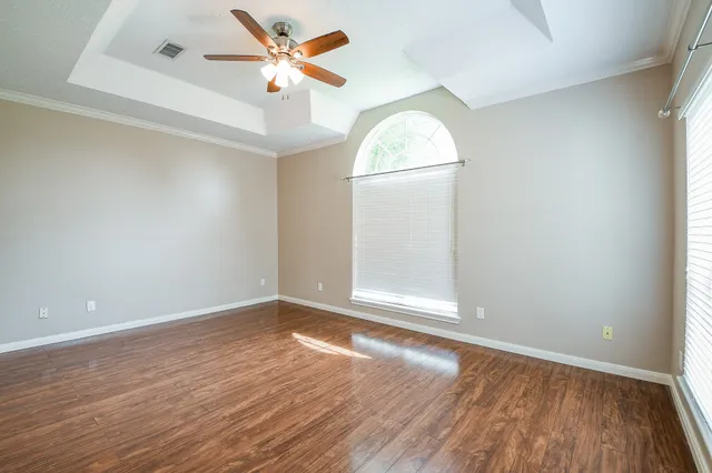an empty room with wooden floor fan and windows