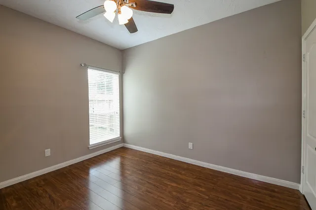 an empty room with wooden floor chandelier fan and windows