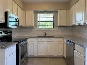 a kitchen with white cabinets appliances a sink and a window