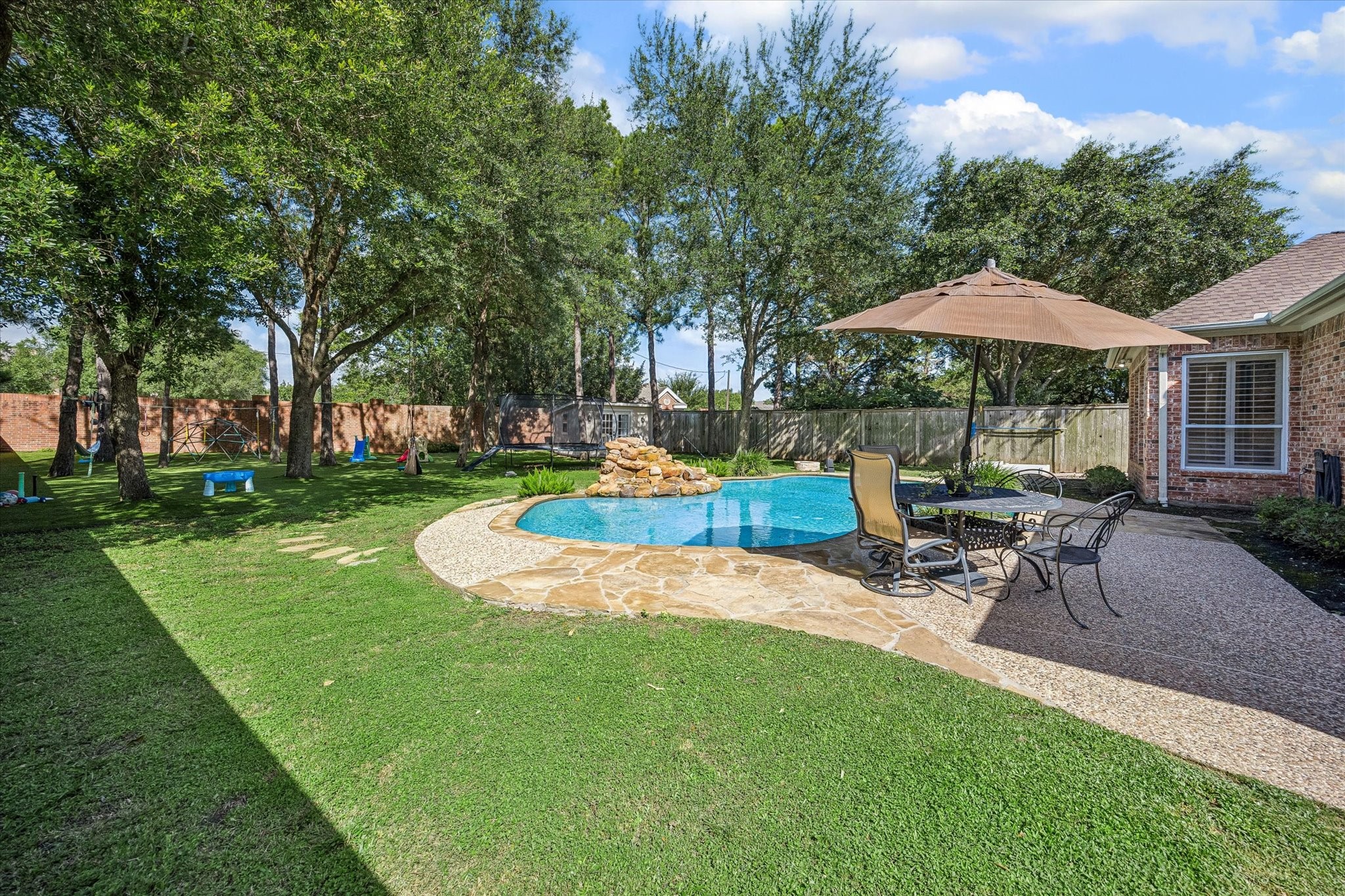 3047 Bonnebridge Way Boulevard Houston, TX 77082 - Photo 22 of 50 Resort-style backyard featuring a sparkling pool with a waterfall, a cozy fire pit perfect for family s'mores nights, an expansive kids' play area, a detached casita ideal for a private studio, and multiple lounge areas for entertaining.