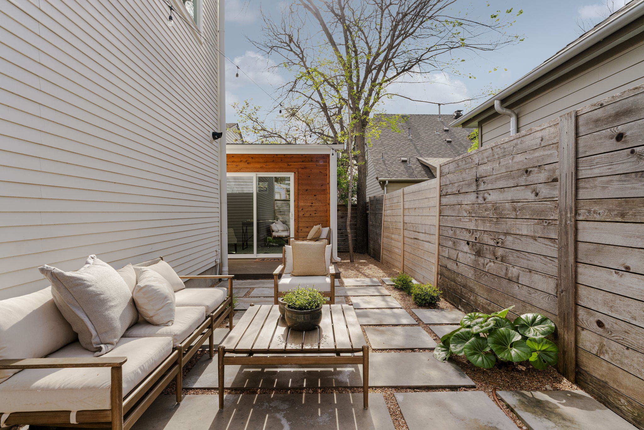 605 Harris Avenue Austin, TX 78705 - Photo 30 of 34 The full backyard picture: a beautifully landscaped patio with large stone pavers, lush plantings, string lights, and the cedar-clad office pod as a focal point. An outdoor room that's genuinely inviting in every season.