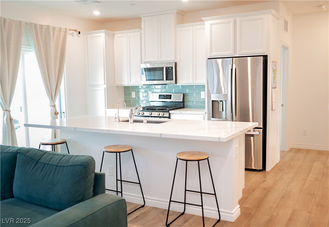 7342 North Decatur Boulevard, Unit 5 North Las Vegas, NV 89084 - Photo 29 of 29 Kitchen featuring appliances with stainless steel finishes, a breakfast bar area, decorative backsplash, open floor plan, and white cabinets
