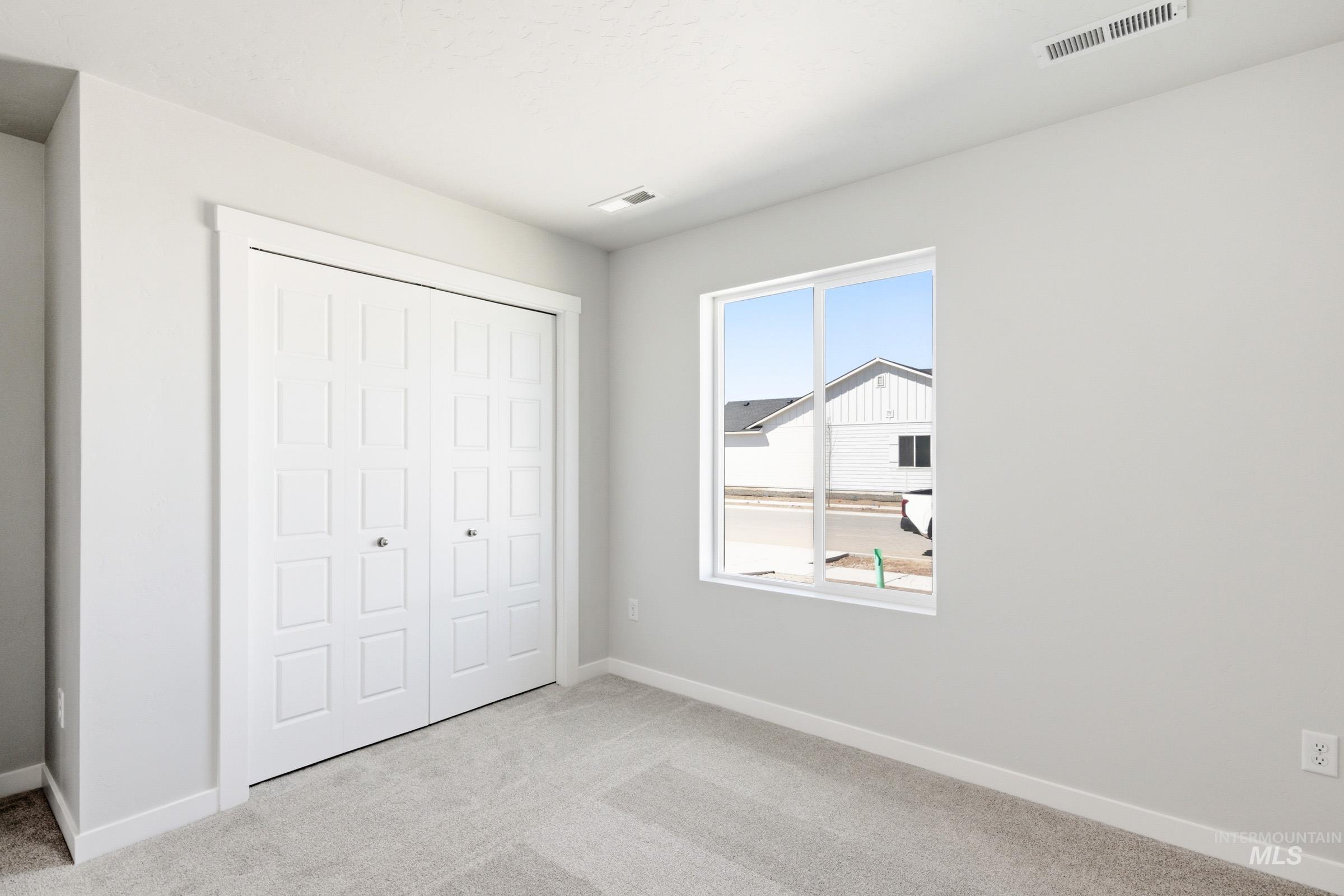 12817 Decatur Street Nampa, ID 83651 - Photo 11 of 19 Bedroom featuring light gray carpeting, a large window, white baseboards, and a bi-fold closet with paneled doors