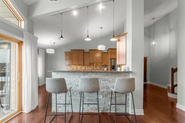 a kitchen with stainless steel appliances kitchen island granite countertop a dining table chairs and a refrigerator