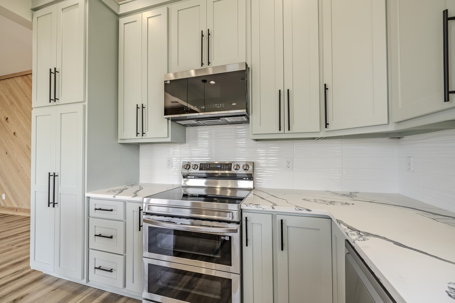 851 Rivers Edge Drive Bath Springs, TN 38311 - Photo 10 of 39 Modern kitchen featuring light-toned cabinetry with black hardware, stainless steel appliances, white subway tile backsplash, and elegant marble-patterned countertops